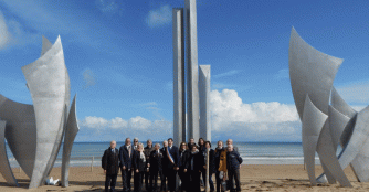 Delegation from Omaha Sister Cities and local leaders stand on Omaha Beach in 2019 in front of the monument, Les Braves