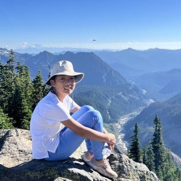 Clair Wang sitting on a rock in front of a mountain range.